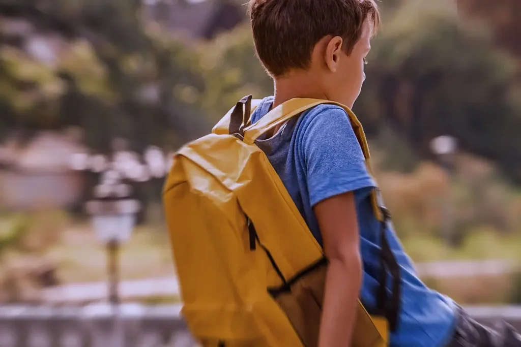 Bambino con zaino seduto su un muretto, guarda in lontananza con un'espressione pensierosa