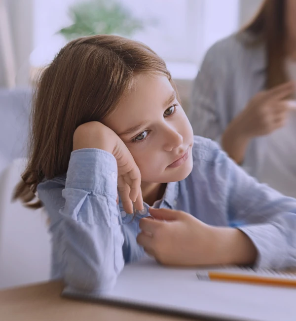 Bambina seduta al banco, in difficoltà a mantenere l’attenzione durante un’attività di classe